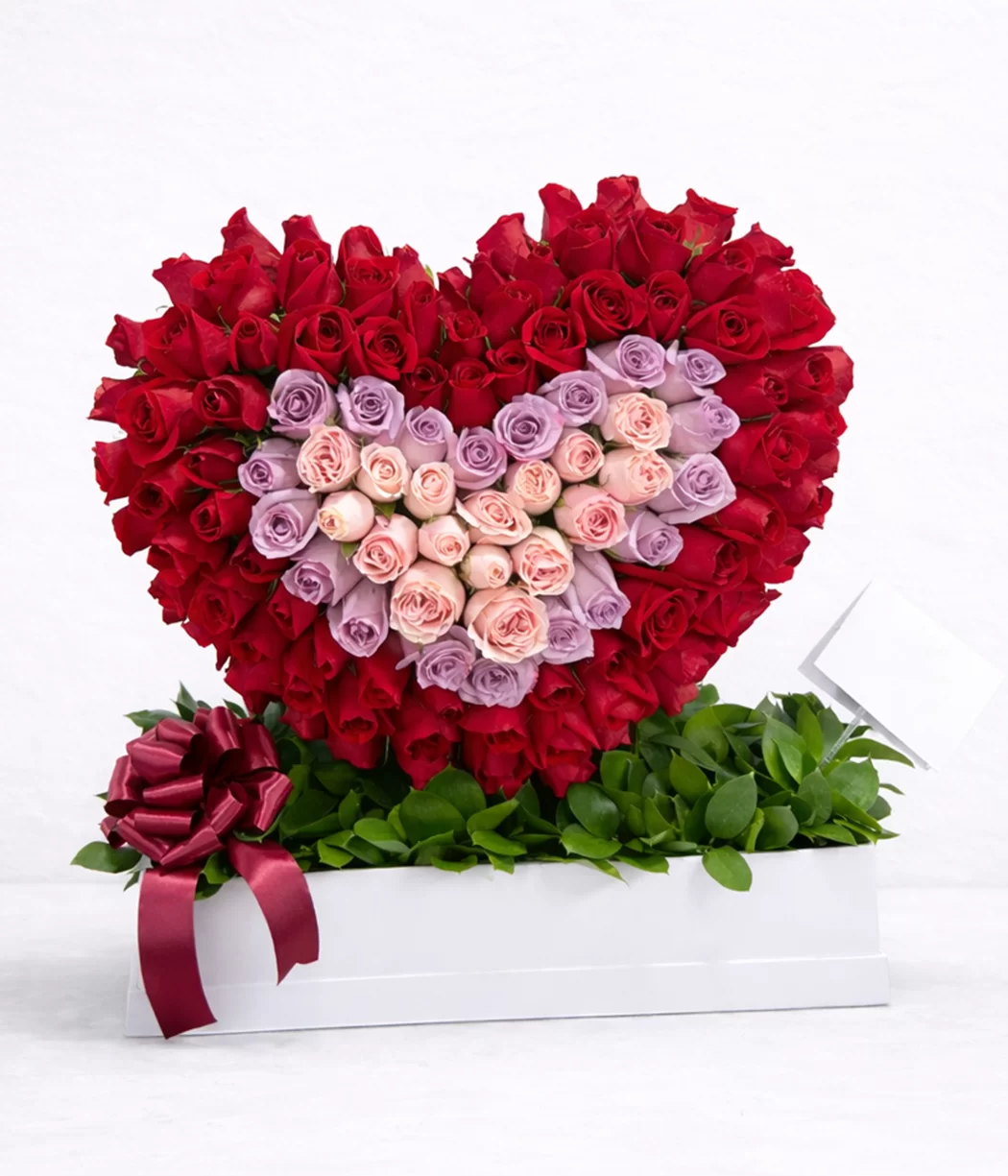 Arreglo floral en forma de corazón con rosas rojas y centro en tonos pastel, ideal para regalar en a